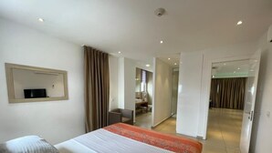 A hotel room with a bed, a mirror, a desk, and a wardrobe. - Apartment With Ocean View (Accra)
