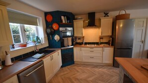 A kitchen with white cabinets, a blue accent wall, a stainless steel refrigerator, and a herringbone wood floor. - Farmhouse with rural and river views & 10 minute walk to market town (Tenbury Wells)