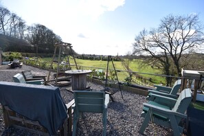 A patio area with outdoor furniture, a swing set, and a view of a green field.