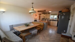 A compact kitchen with a wooden dining table, bench seating, and a refrigerator. - Farmhouse with rural and river views & 10 minute walk to market town (Tenbury Wells)