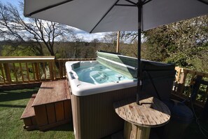 A hot tub with a wooden deck and a table under a canopy.
