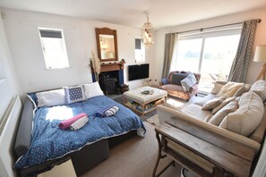 A well-lit room with a bed, a sofa, a wooden table, and a TV.