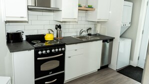 Una cocina compacta con armarios blancos, una estufa negra, un lavamanos y un lavavajillas.