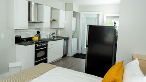 Una cocina compacta con armarios blancos, un refrigerador negro, una estufa y un microondas.