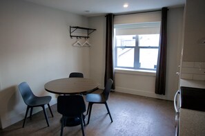 Une pièce comprenant une table ronde, quatre chaises, une fenêtre avec des rideaux et une étagère fixée au mur, dotée de supports pour suspendre des vêtements.
