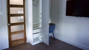 Une pièce avec une porte en bois, une armoire blanche dotée de plusieurs étagères, une chaise bleue et un téléviseur fixé au mur.