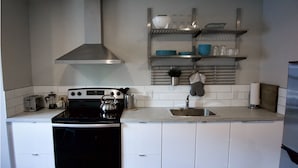 Une cuisine compacte équipée d’une cuisinière, d’un évier et d’étagères en acier inoxydable au-dessus du plan de travail.
