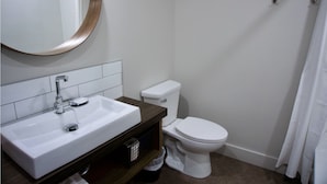 Une salle de bain avec un lavabo blanc, un miroir rond, des toilettes et un rideau de douche.