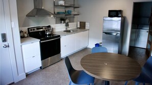 Une cuisine compacte avec des meubles blancs, une cuisinière en acier inoxydable, un four à micro-ondes et un évier. On y trouve une table ronde en bois et deux chaises.