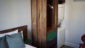 Una camera d'albergo con un letto, un armadio in legno, una lavatrice bianca e una sedia rossa.