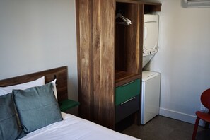 A hotel room with a bed, a wooden wardrobe, a white washing machine, and a red chair. - Welcome to style and elegance (Edmundston)