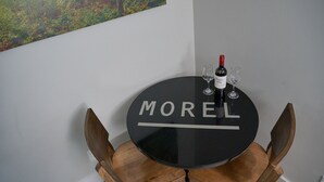 Een ronde, zwarte tafel met de tekst 'MOREL', vergezeld van twee wijnglazen en een fles wijn.