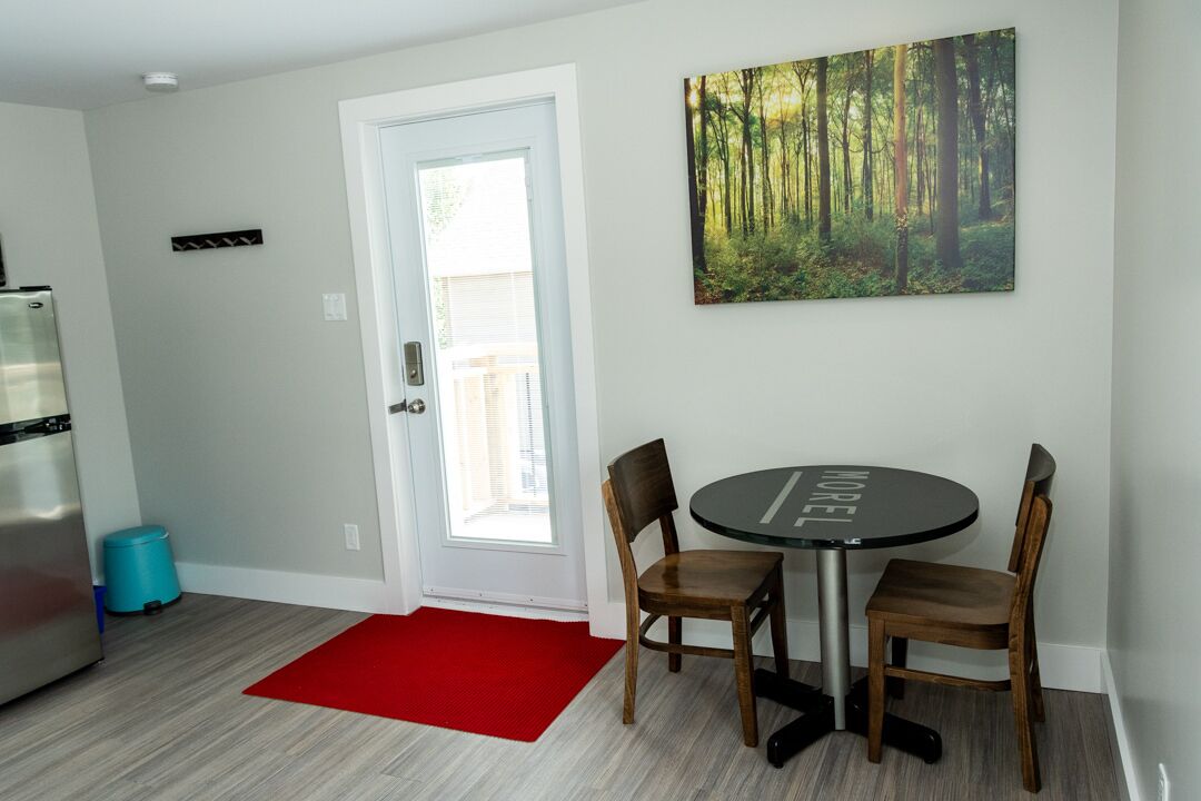 Une cuisine moderne avec un réfrigérateur en acier inoxydable, un tapis rouge et un coin repas comprenant une table ronde et deux chaises.