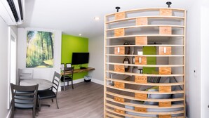 Une pièce avec une bibliothèque en bois aux lignes courbes, une table à manger avec des chaises, un mur d’accent vert et un téléviseur à écran plat.