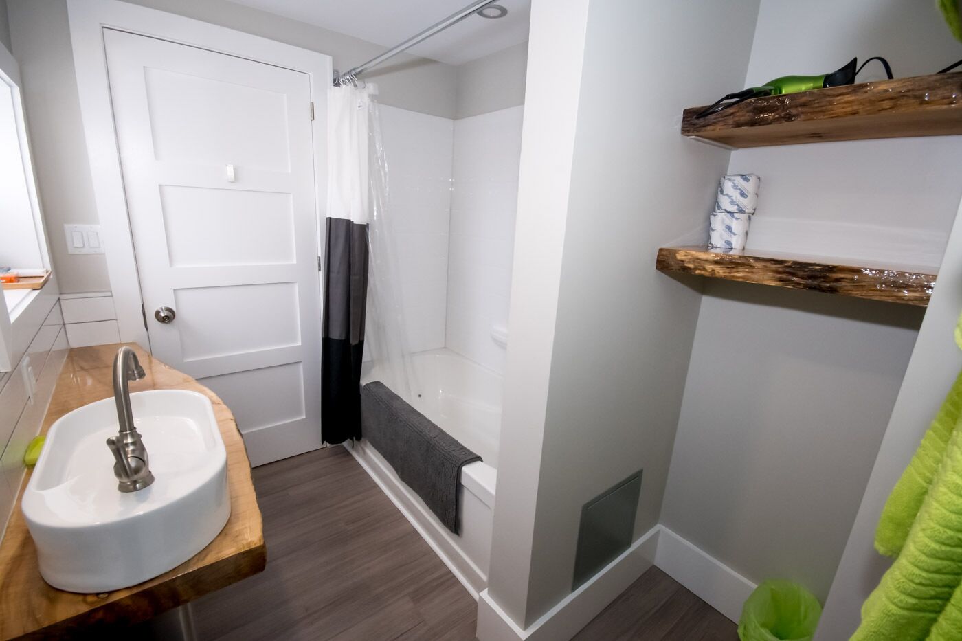 Un baño con lavamanos blanco, cortina de ducha, bañera y estantes de madera.