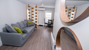 Un salon moderne avec un canapé gris, un plancher en bois et un miroir incurvé original.