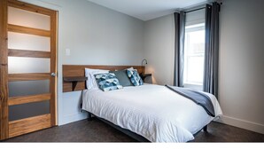 Un dormitorio con cama, mesita de noche, armario de madera y ventana con cortinas.