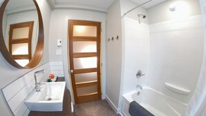 Un baño con un lavamanos blanco, un espejo, una puerta de madera y una bañera blanca.