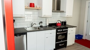 Una cocina moderna con armarios blancos, encimera negra, campana extractora de acero inoxidable, hervidor rojo y lavavajillas.