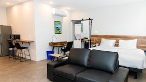 Ein modernes Hotelzimmer mit einer schwarzen Ledersofa, einem Bett mit weißen Leinen, einem Schreibtisch mit Computer, einer Mikrowelle und einer kleinen Küchenzeile.
