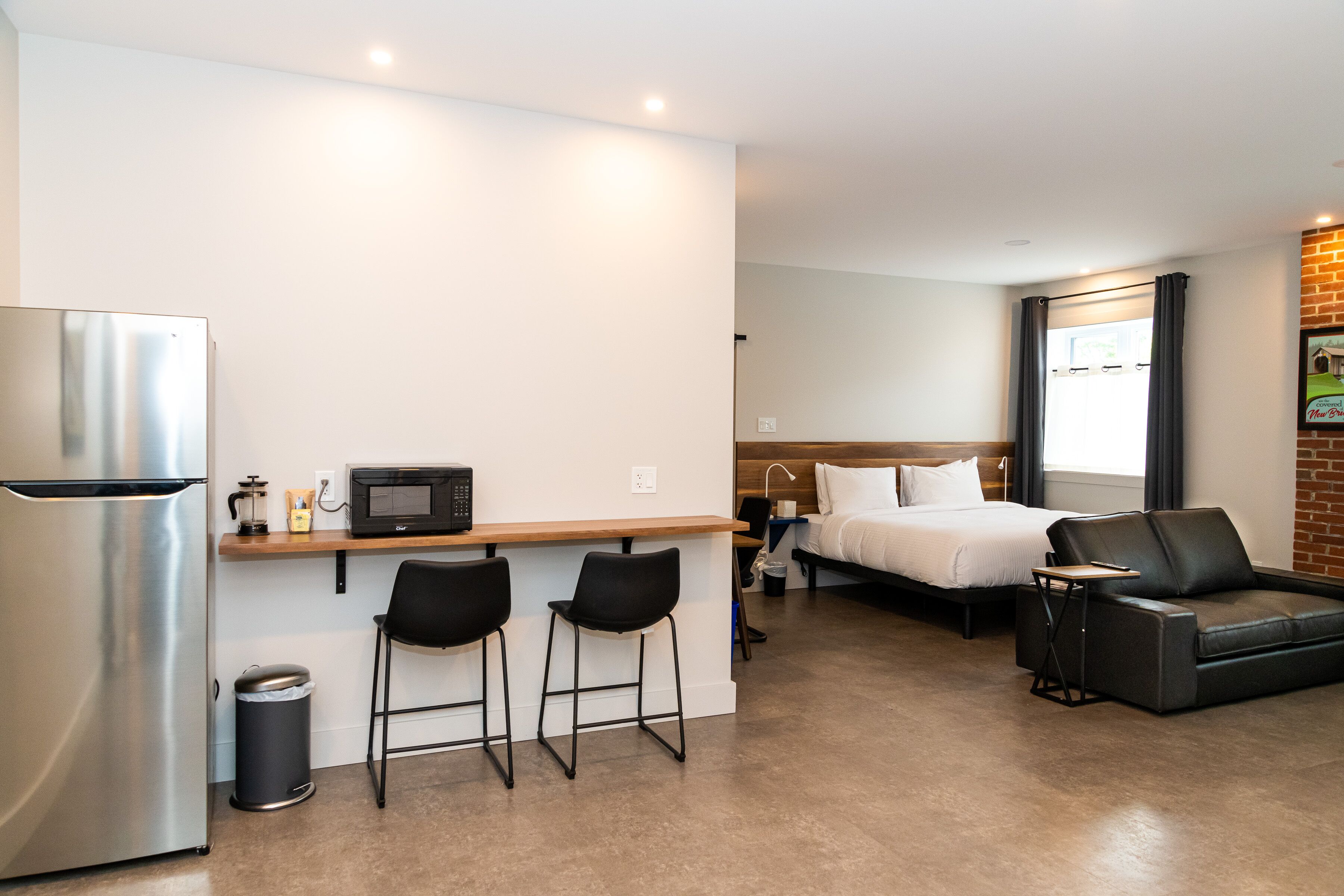 A compact hotel room with a kitchenette, a bed, a sofa, and a small bar area.