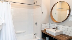 Un baño moderno con bañera, ducha, lavabo con espejo y un perchero para toallas.