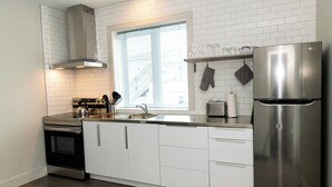Una cocina moderna con armarios blancos, electrodomésticos de acero inoxidable y un ventanal que proporciona luz natural.