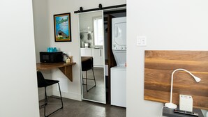 Cocina compacta con microondas, tostadora y cafetera, una silla negra y una mesa de comedor de madera.