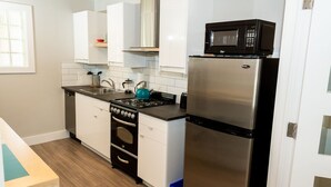 Une cuisine compacte avec des meubles blancs, un réfrigérateur en acier inoxydable, un four à micro-ondes, une cuisinière et un évier.