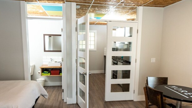 Une chambre moderne comprenant un lit, une table à manger avec des chaises, un coin cuisine et une salle de bain avec un miroir et des toilettes.