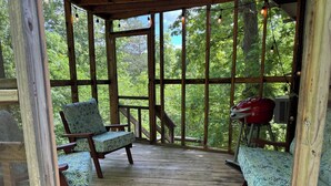 A covered porch with wooden flooring, two patterned chairs, and a red grill. - Roundhouse Cabin in Pigeon Forge …in town  (Pigeon Forge)