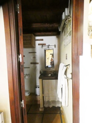 Ein schmaler Flur führt zu einem Badezimmer mit Waschbecken, Spiegel und Handtuchhalter.