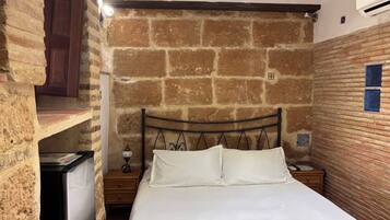 Una cama individual con ropa de cama blanca en una habitación con paredes de ladrillo visto y techo de madera.