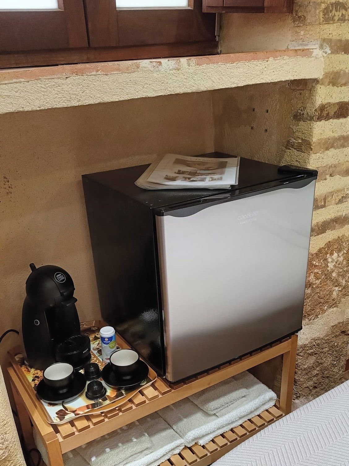 A compact kitchenette with a refrigerator, a coffee maker, and a tray with cups and a small container.