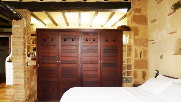 A bedroom with a large wooden wardrobe, a bed, and a stone wall.