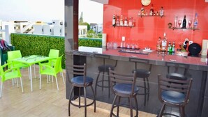 Een bar met een rode wand van tegels, barstoelen en een toonbank vol flessen en glazen.