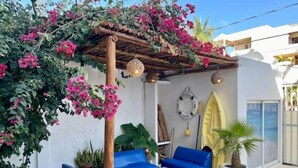 Een overdekt terras met blauwe banken, een tafel en een potplant.
