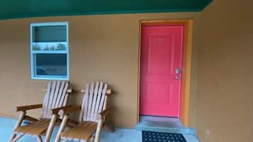 A building with a red door, two wooden chairs outside, and a small window.