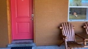 Une porte rouge portant le numéro 2, un banc en bois et une fenêtre donnant sur des arbres.