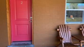 A red door with the number 2, a wooden bench, and a window with a view of trees.