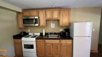 A compact kitchen with wooden cabinets, a white refrigerator, a stove, a microwave, and a sink.