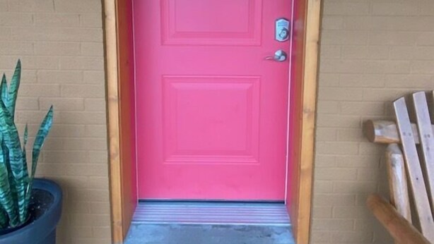 Una puerta rosa con el número 4, una planta en maceta y un banco de madera.