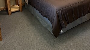Ein Schlafzimmer mit Holz-Kopfteil, einem Bett mit brauner Bettdecke, einem Nachttisch mit Lampe und einem kleinen Tisch.