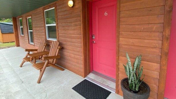 Eine Holzhütte mit roter Tür, einem Blumentopf und zwei Holzstühlen auf der Veranda.