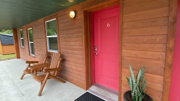 A wooden cabin with a red door, a potted plant, and two wooden chairs on the porch.