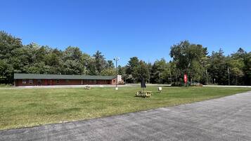 A red building with a green roof, a grassy field, and a paved road.