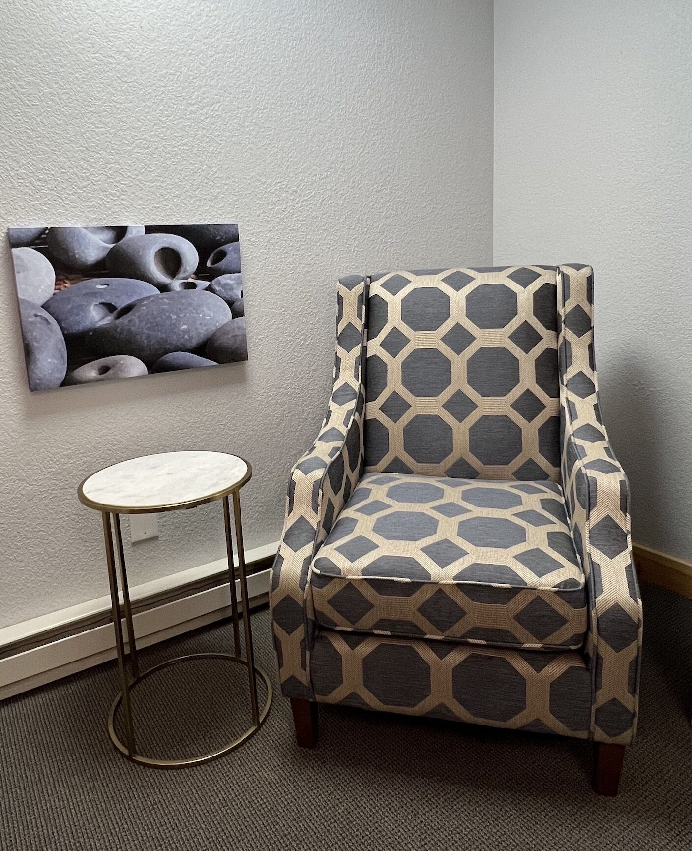 Une pièce d’angle avec un fauteuil à motifs, une petite table ronde et un tableau accroché au mur.