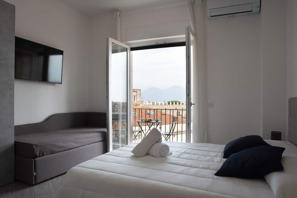 A hotel room with a bed, a sofa, and a balcony with a table and chairs.