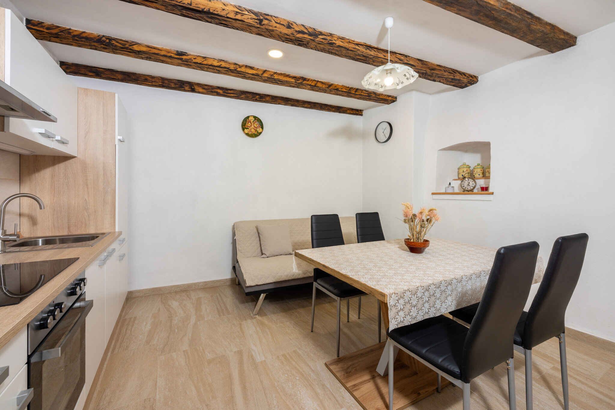 Een kleine keuken met moderne apparaten, een zithoek met tafel en stoelen, en een houten plafond.