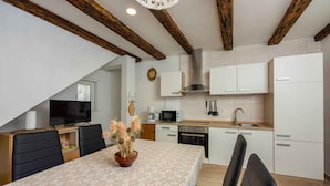 A modern kitchen with white cabinets, a microwave, and a stove. There is a dining table with chairs and a decorative vase.